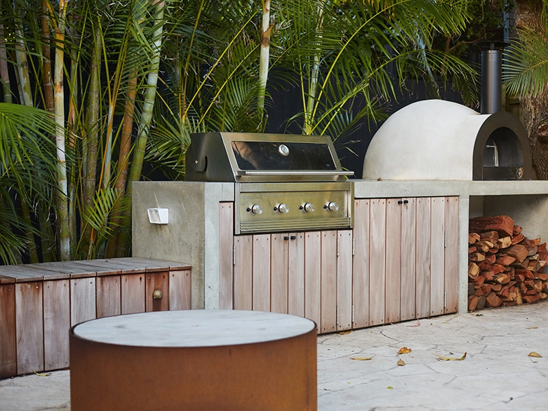 A grill, a wooden table, and a bench, set for an outdoor dining experience