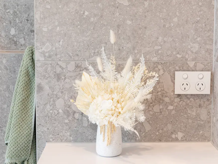 White vase filled with white flowers on a counter.