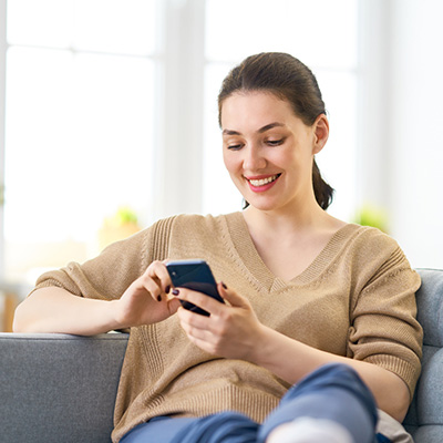 Woman happily seated on a couch, holding a phone in her hand.