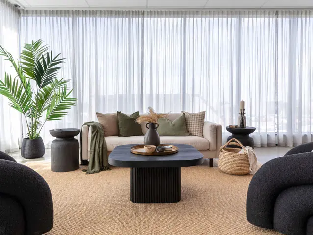 A modern living room with sleek black furniture and a large window, allowing natural light to illuminate the space.