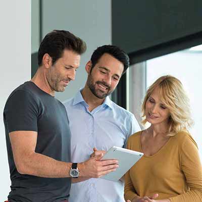 A group of three people standing in an office, analyzing a tablet.