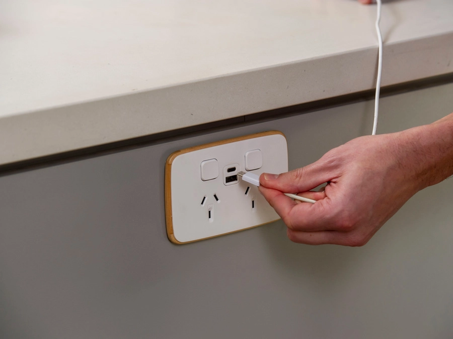 A hand plugging a type-c cable into a wall socket with electrical outlets and USB ports