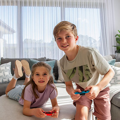 Two children happily playing video games on a couch with a gaming controller