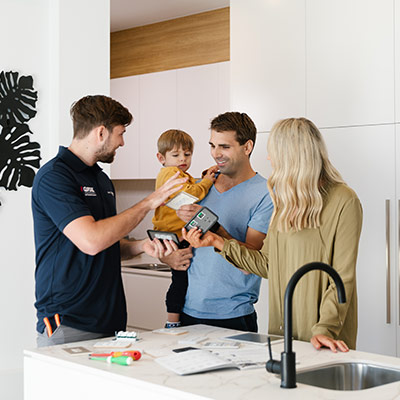 A family in conversation with a Clipsal electrician in their kitchen, with the father holding his son in his arms