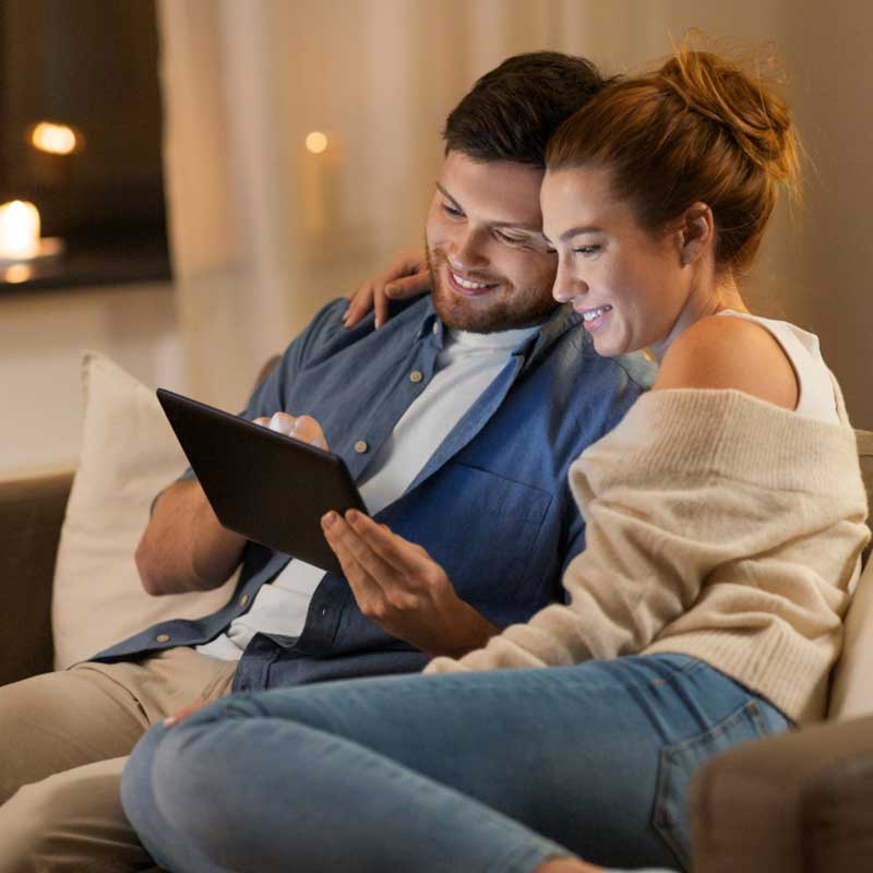 Couple sitting on a couch, holding a tablet device