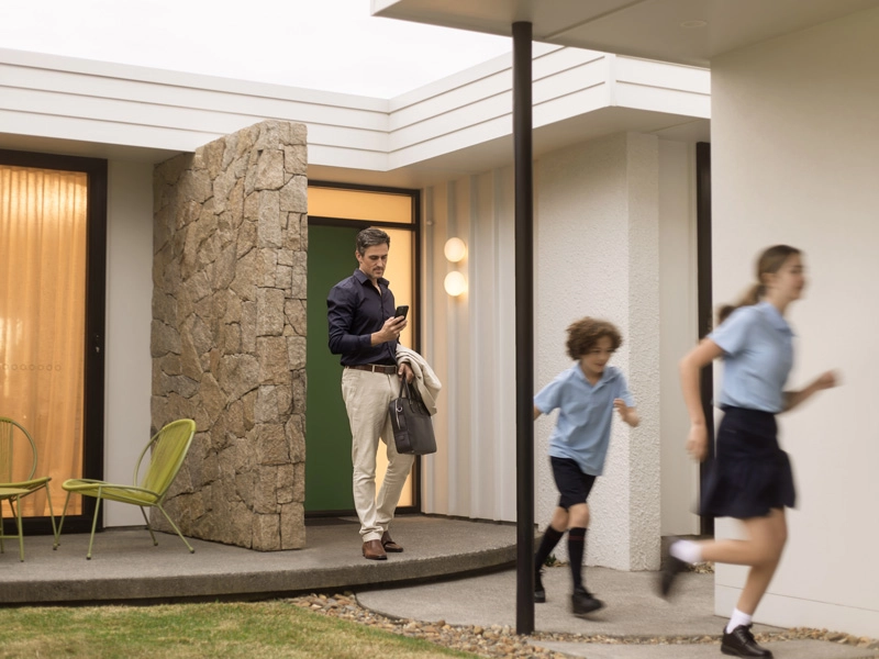 Man walks alongside two children outside a house